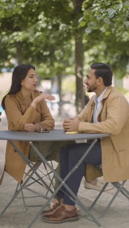 Video-Vertical-De-Una-Pareja-Musulmana-En-Una-Cita-Sentada-En-Una-Mesa-Al-Aire-Libre-En-Una-Calle-De-La-Ciudad-Hablando-Juntos-1